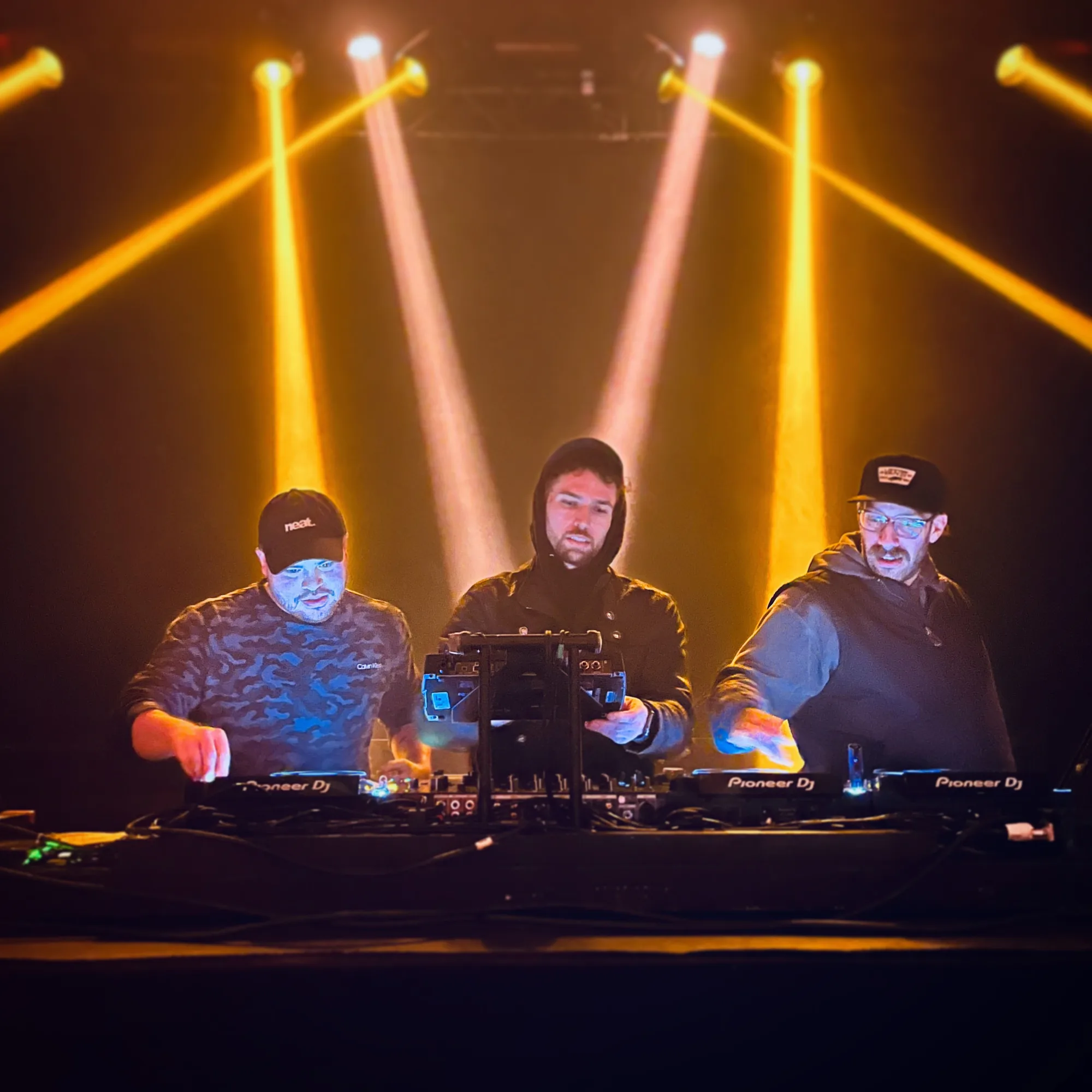 DJ trio under amber stage beams